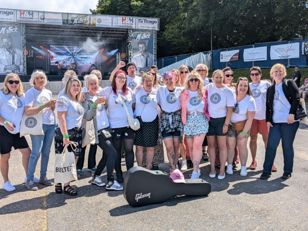 Linda with a large group of women in matching white t-shirts at an outdoor music festival